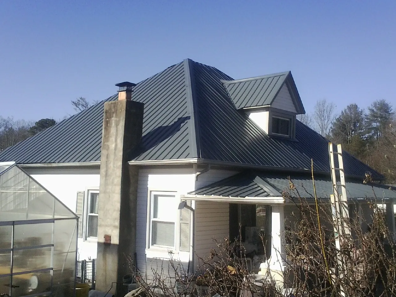 Dark blue standing seam metal roof on a white farmhouse with dormer — Slate & Tile Roof Repair by Roofing Brothers in Keuka Park