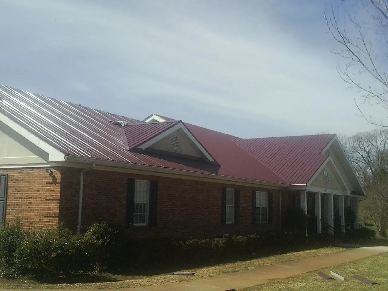 Red metal roof with gabled entries on a long brick building, from a Hail Damage Roof Repair job in Keuka Park