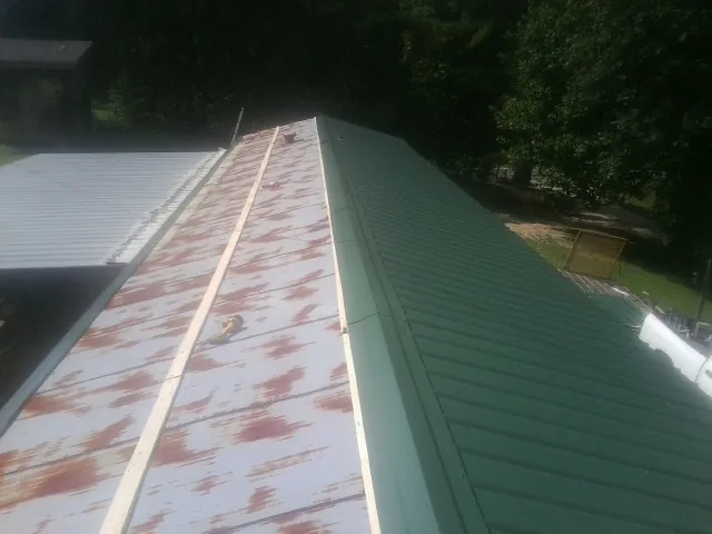 Old rusted panels beside newly installed green metal roofing — Wind Damage Roof Repair by Roofing Brothers in Keuka Park