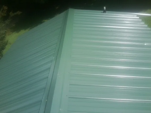 New green metal panels meeting at the ridge of a roof — Flat Roof Repair work by our crew in Keuka Park