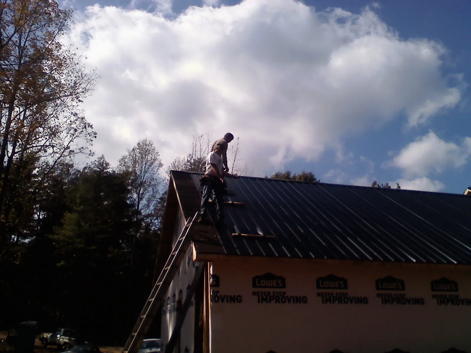 Roofer fastening dark metal panels high against a cloudy sky, from a Roof Inspection job in Keuka Park