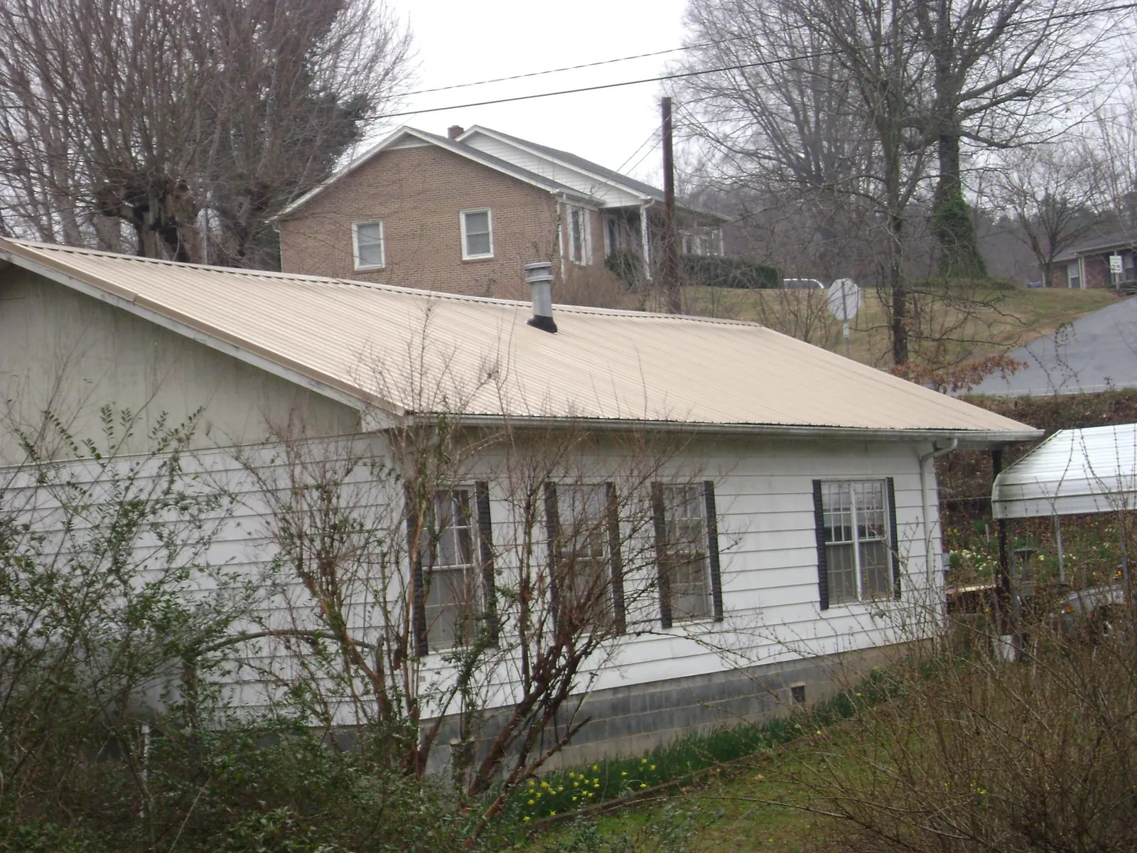 Tan metal roof on a white sided house set into a hillside — Commercial Roofing by Roofing Brothers in Keuka Park