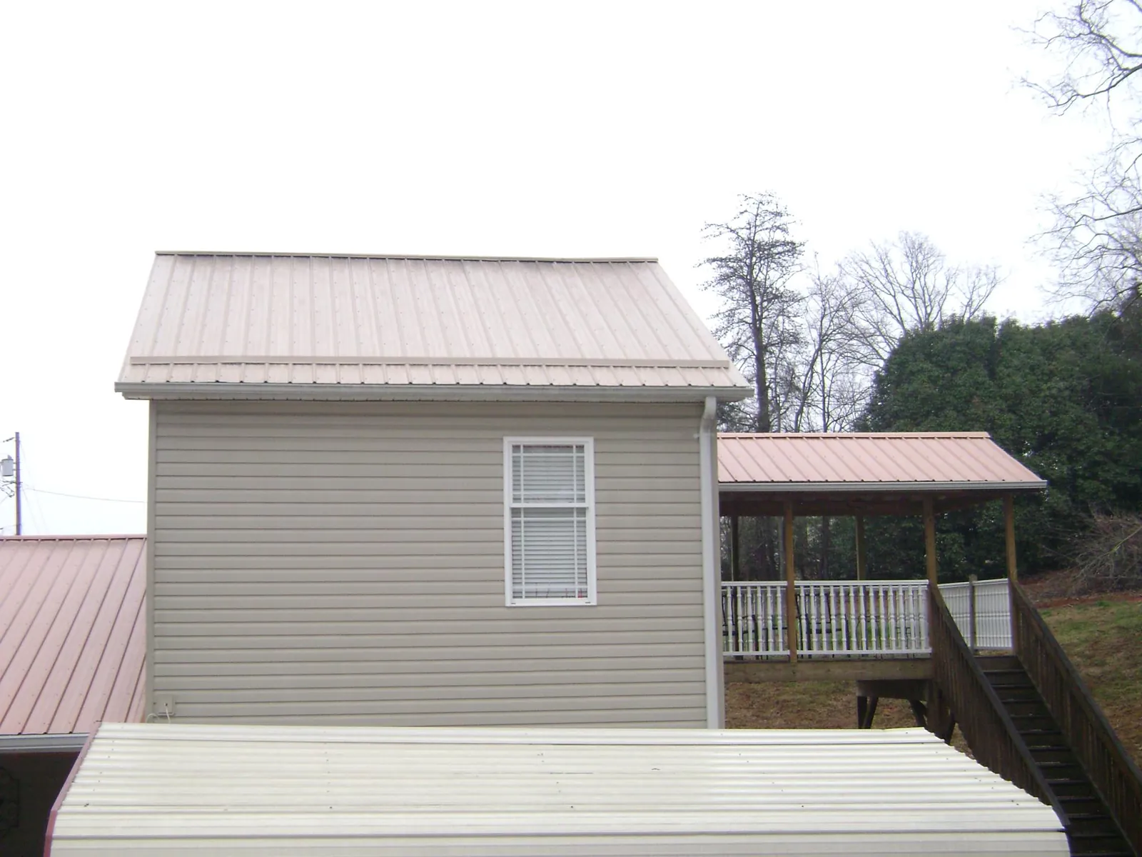 Tan metal roofs on a two story addition and attached porch, from a Roof Replacement job in Keuka Park